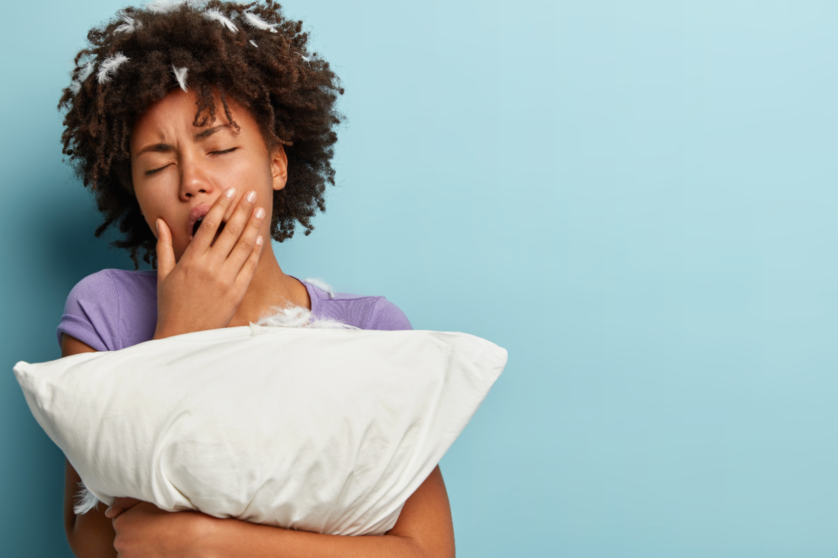 Ganhar dinheiro dormindo Mulher jovem segurando travesseiro branco e bocejando, com fundo azul claro