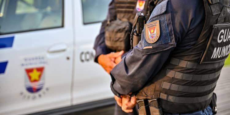 Dois agentes da Guarda Civil Municipal de Vitória próximos a viatura oficial com uniforme preto