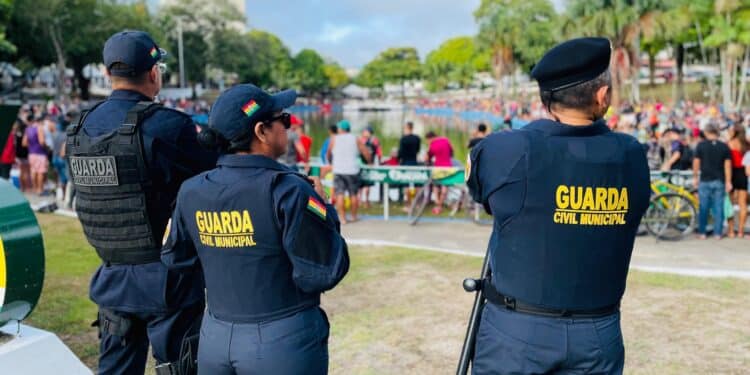 Três agentes da Guarda Civil Municipal vigiam evento ao ar livre com público numeroso em área gramada