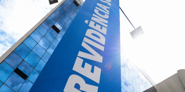 Placa azul grande com texto branco escrito Previdência Social em frente a prédio moderno de vidro