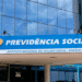 Fachada do Instituto Nacional do Seguro Social com logo e nome Previdência Social em prédio moderno com vidro refletindo o céu