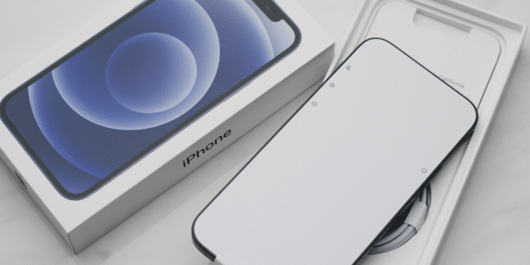 iPhone 12 preto com tela branca dentro da caixa ao lado da embalagem com imagem do aparelho