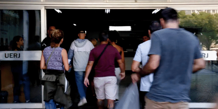 Grupo de pessoas caminhando para dentro de um edifício com a placa UERJ na porta de vidro