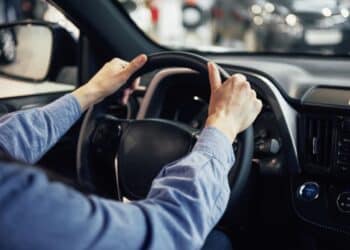 Mãos no volante de um carro com câmbio manual, representando o ato de fazer a meia embreagem.