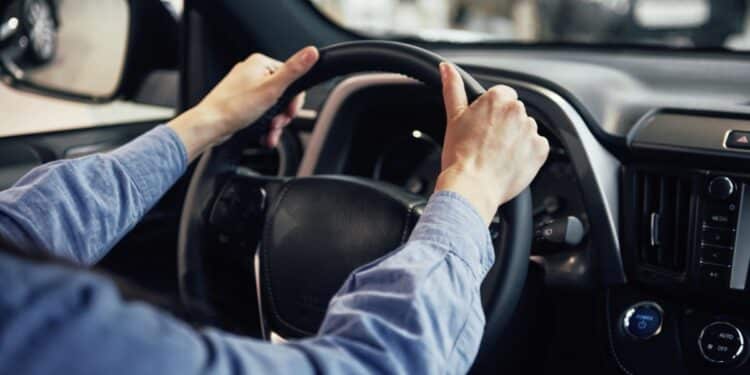Mãos no volante de um carro com câmbio manual, representando o ato de fazer a meia embreagem.