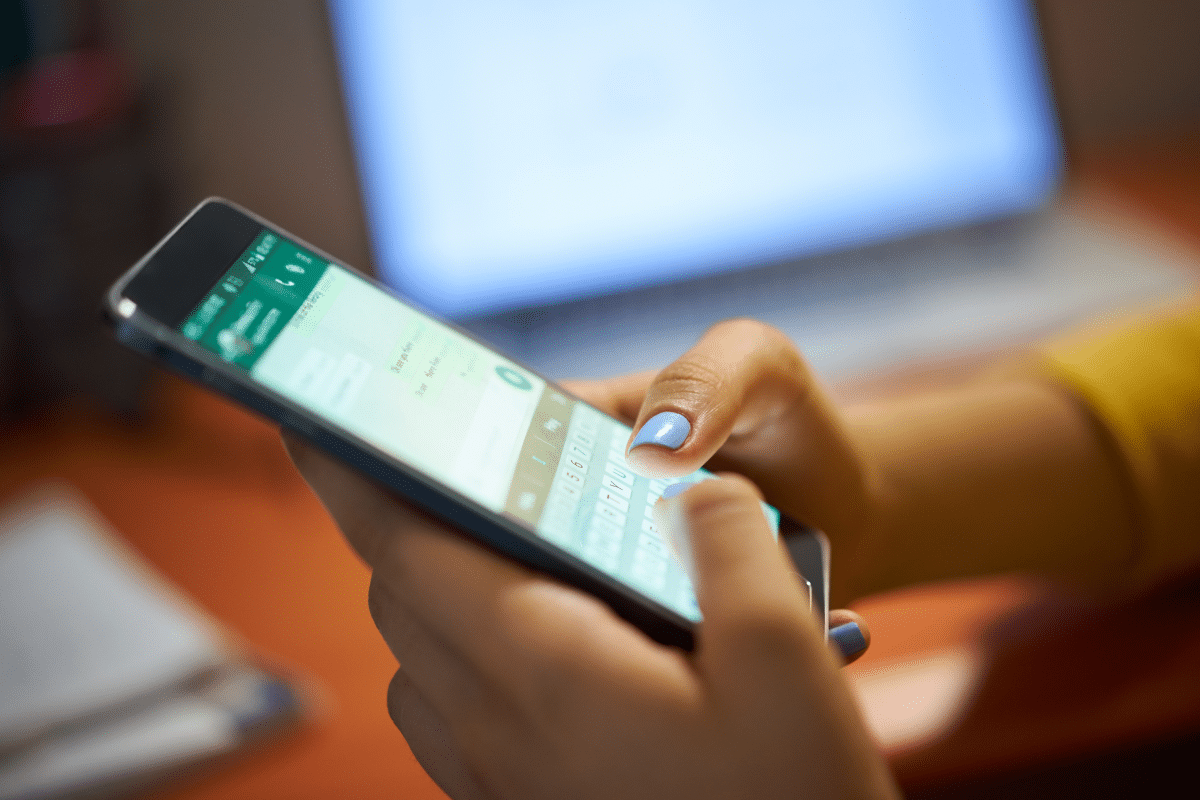 Mãos femininas com unhas pintadas digitando mensagem no aplicativo WhatsApp em smartphone