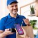 Entregador sorridente com uma maquininha de cartão, enquanto um cliente aproxima o smartphone para efetuar um pagamento por aproximação, representando a conveniência dos aplicativos de delivery.