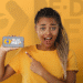 Mulher surpresa com tranças apontando para celular exibindo o app Pé de Meia em fundo amarelo.