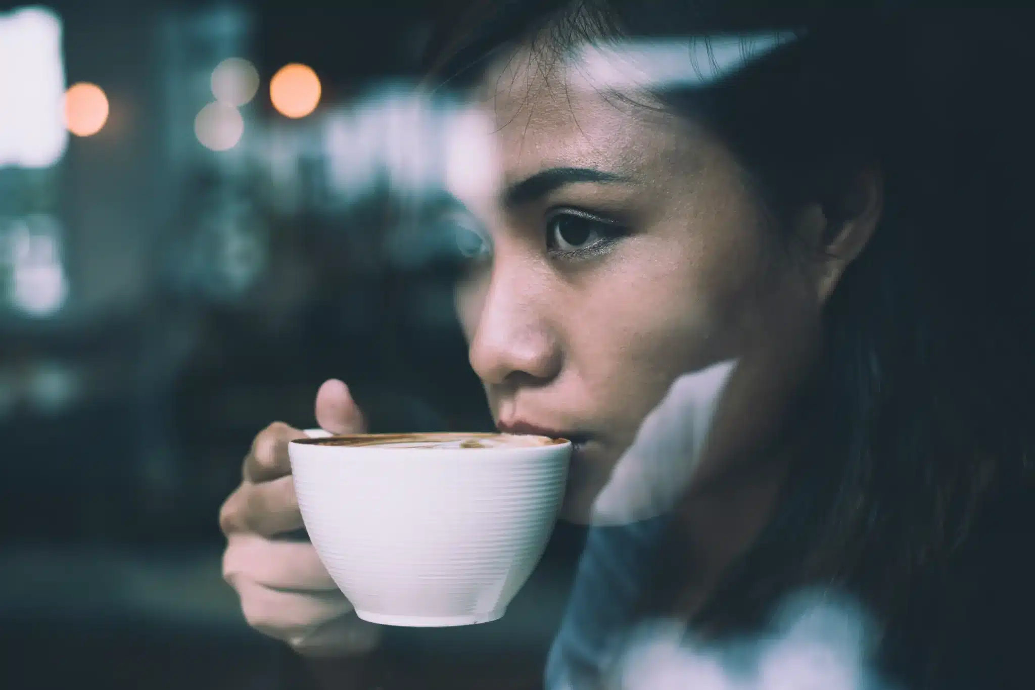 Consumo de café Mulher bebendo café pensativa em um ambiente aconchegante, refletida em uma janela.