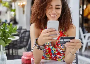 Mulher sorrindo enquanto faz pagamento online com cartão de crédito e celular, representando a comparação entre formas de pagamento como o Pix parcelado e o cartão de crédito.