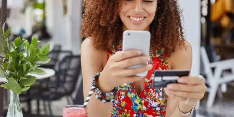 Mulher sorrindo enquanto faz pagamento online com cartão de crédito e celular, representando a comparação entre formas de pagamento como o Pix parcelado e o cartão de crédito.