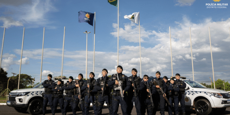 Grupo de policiais militares do Distrito Federal posando em formação com armas e viaturas ao fundo
