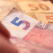 Notas de real brasileiro, com destaque para a nota de 5 reais e notas de 50 reais ao fundo.