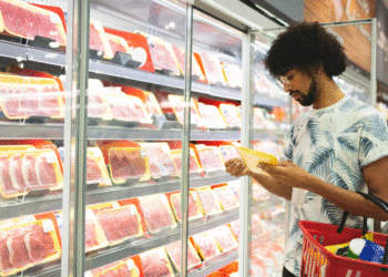 Homem segurando cesto de compras verifica embalagem de carne em display refrigerado de supermercado