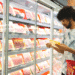 Homem segurando cesto de compras verifica embalagem de carne em display refrigerado de supermercado