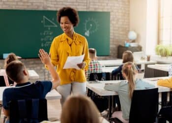 Professora sorrindo em sala de aula, ensinando alunos, representando a importância da Carteira Nacional do Professor de 2025.