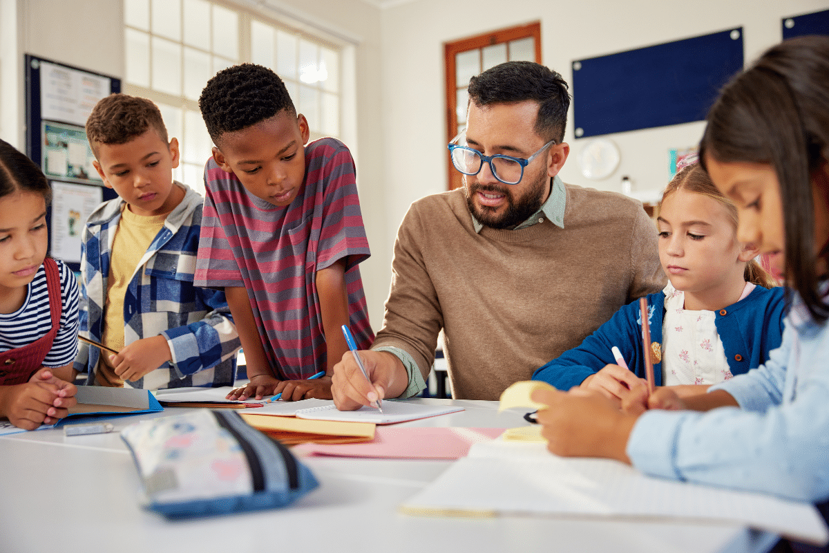 Educador ajudando crianças com tarefa enquanto estudam juntas em sala de aula