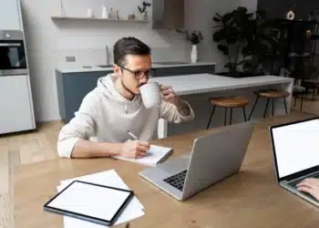 Homem trabalhando de casa com laptop e caderno, refletindo as profissões remotas em alta no mercado.