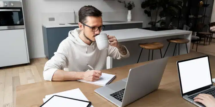Homem trabalhando de casa com laptop e caderno, refletindo as profissões remotas em alta no mercado.