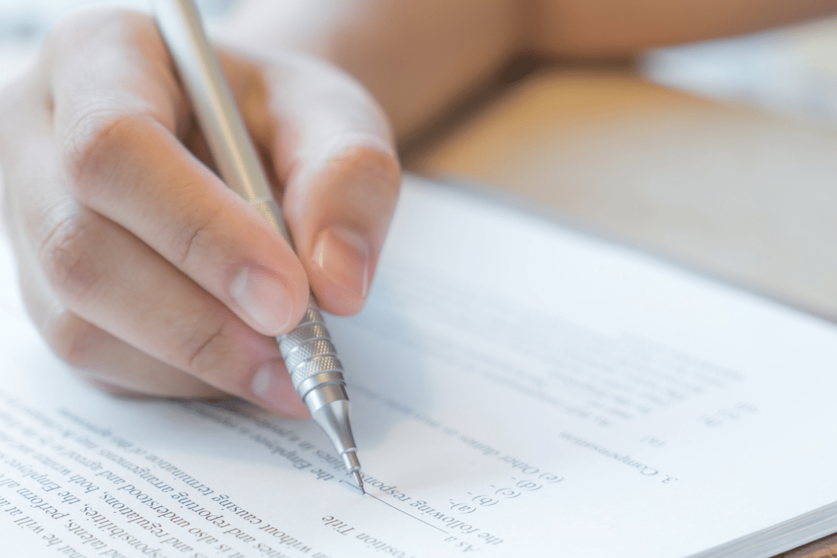 Mão segurando lapiseira a escrever em papel com texto e perguntas impressas