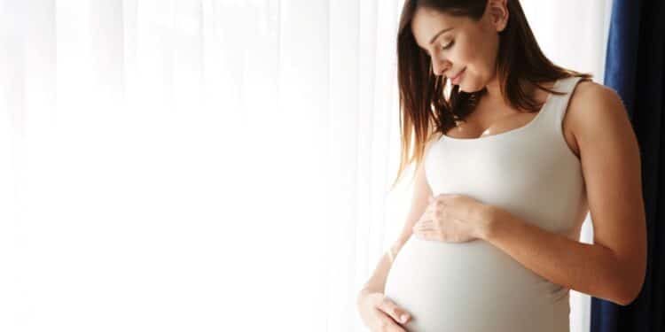 Mulher grávida com a mão na barriga sorri, ilustrando a discussão sobre paracetamol e risco de autismo em estudos científicos