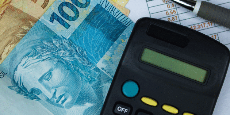 A imagem mostra várias cédulas de real ao lado de uma calculadora preta e uma caneta prata, colocadas sobre uma planilha com números e valores. A cena representa o cálculo financeiro, gerenciamento e planejamento econômico.