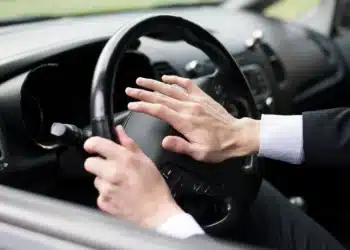 Homem com terno segurando o volante e buzinando no carro, ilustrando o que pode acontecer se você buzinar sem motivo em algumas cidades.