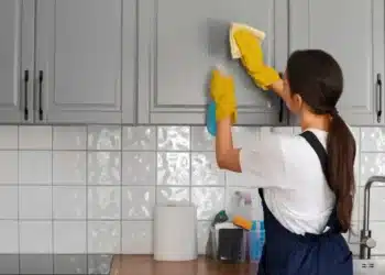 Mulher limpando armário de cozinha com produtos de limpeza, com foco em tarefas domésticas.