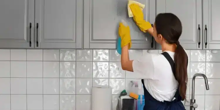 Mulher limpando armário de cozinha com produtos de limpeza, com foco em tarefas domésticas.