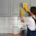Mulher limpando armário de cozinha com produtos de limpeza, com foco em tarefas domésticas.