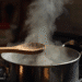 Panela de inox com vapor saindo e colher de pau sobre fogão aceso em cozinha