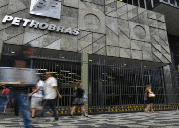 Fachada da sede da Petrobras com letreiro, grades e pessoas andando em frente em rua calçada