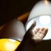 Mão de uma pessoa alcançando uma lâmpada LED acesa em um lustre, simbolizando a economia de energia e o acesso à luz gratuita do programa Luz do Povo.