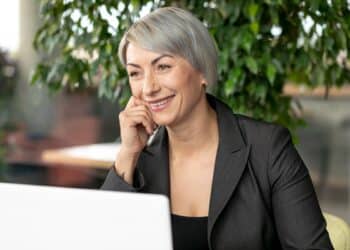 Executiva madura com cabelo grisalho em blazer preto sorrindo confiante em escritório com plantas representando oportunidades Carrefour 50+