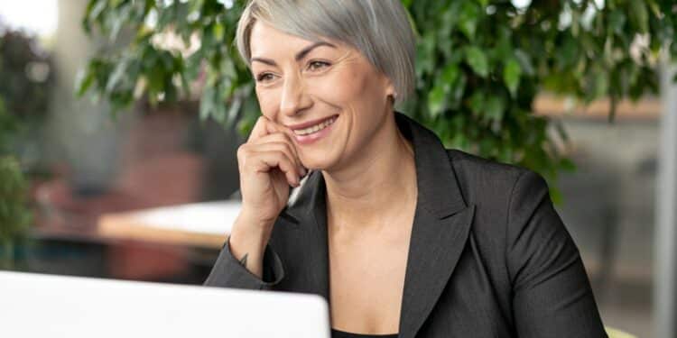 Executiva madura com cabelo grisalho em blazer preto sorrindo confiante em escritório com plantas representando oportunidades Carrefour 50+