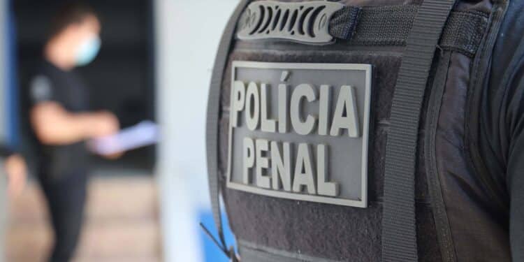 Close do colete tático preto da Polícia Penal com identificação oficial durante operação no sistema prisional