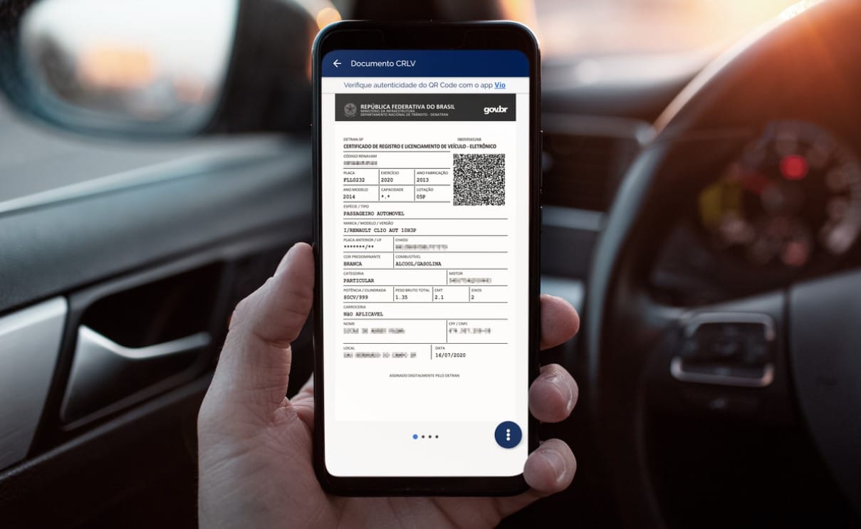 Mão de motorista segurando um celular com a tela exibindo o Certificado de Registro e Licenciamento de Veículo Eletrônico (CRLV-e) com o QR Code, dentro de um carro. Ilustra a versão digital oficial de um documento que golpistas tentam falsificar.