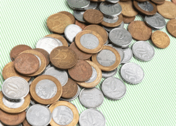 Várias moedas do Plano Real espalhadas em uma superfície listrada, destacando a possibilidade de encontrar moedas raras no troco.