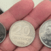 Três moedas antigas de 10, 20 e 50 Cruzeiros do ano de 1986, sendo seguradas na palma da mão, em estado de Flor de Cunho. Imagem ilustra a raridade das moedas de baixa tiragem procuradas por colecionadores de numismática.