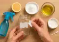 Pessoa removendo um rótulo de frasco de vidro com algodão e ingredientes naturais como limão, óleo e bicarbonato