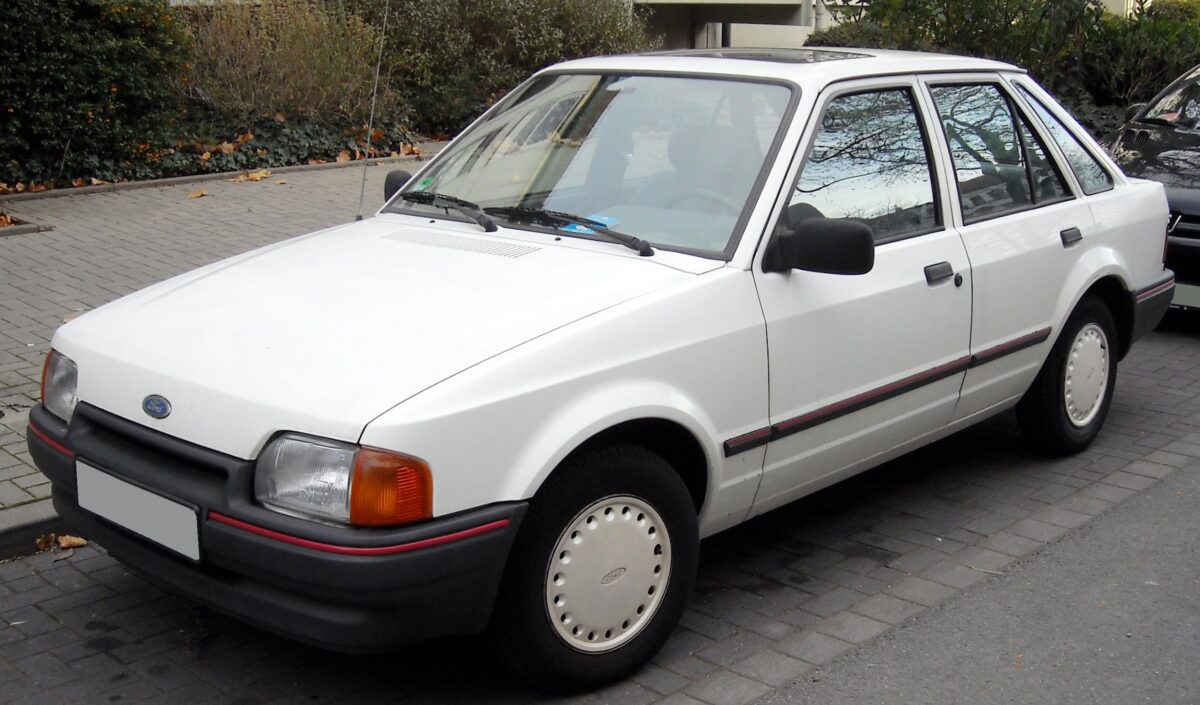 Carro Ford Escort branco modelo antigo estacionado na rua com pneus e vidros transparentes