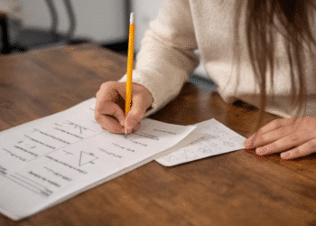 Pessoa realizando prova escrita sobre a mesa de madeira.
