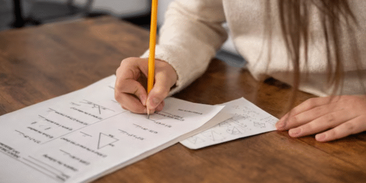 Pessoa realizando prova escrita sobre a mesa de madeira.