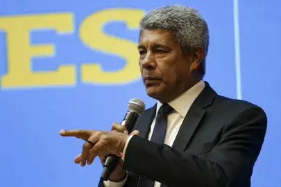 Homem de terno segurando microfone e apontando durante discurso em evento