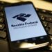 Aplicativo da Receita Federal exibindo o serviço “Meu Imposto de Renda” em um celular sobre o teclado de computador.