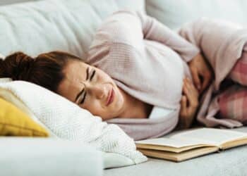 Mulher deitada no sofá com expressão de dor abdominal, segurando a barriga.