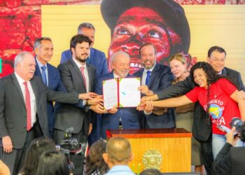 Autoridades governamentais em cerimônia oficial segurando documento de lei sobre energia elétrica gratuita assinado