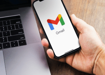 Pessoa segurando celular com o aplicativo Gmail aberto ao lado de um notebook
