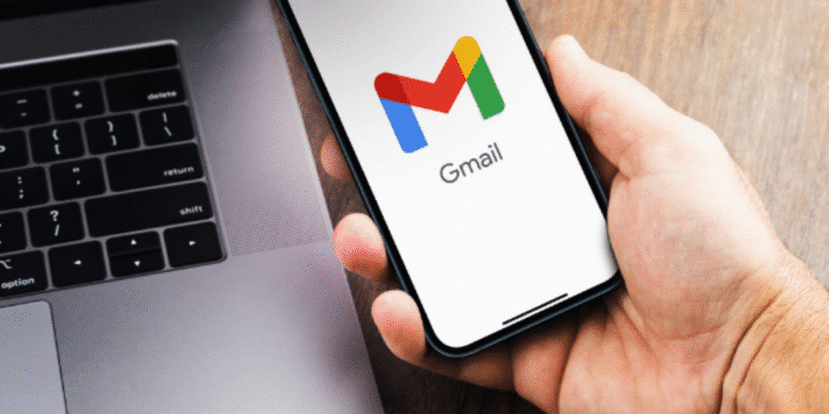 Pessoa segurando celular com o aplicativo Gmail aberto ao lado de um notebook