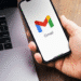 Pessoa segurando celular com o aplicativo Gmail aberto ao lado de um notebook